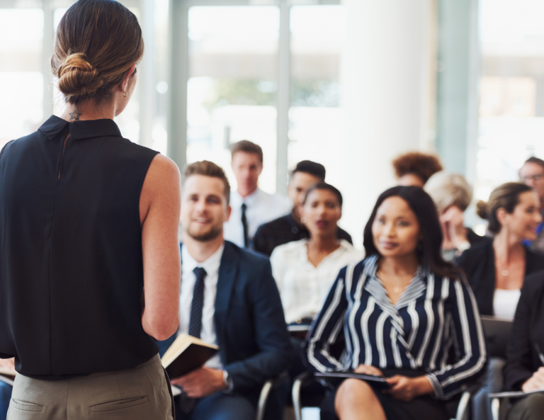 A room full of business professionals is sitting in front of a speaker.