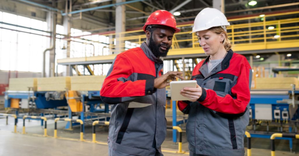 Multi-ethnic coworkers in hardhats using tablet while discussing manufacturing issues at construction plant