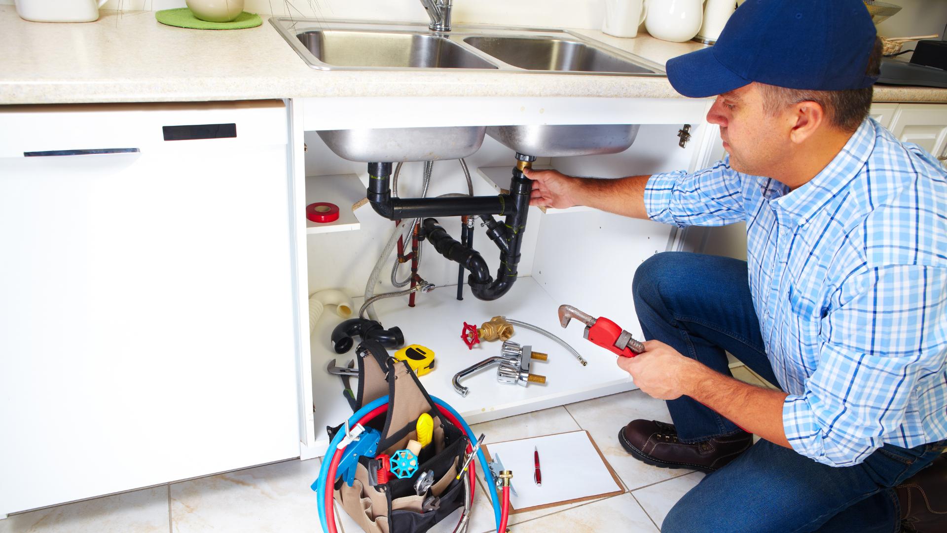 A plumber making repairs under a sink