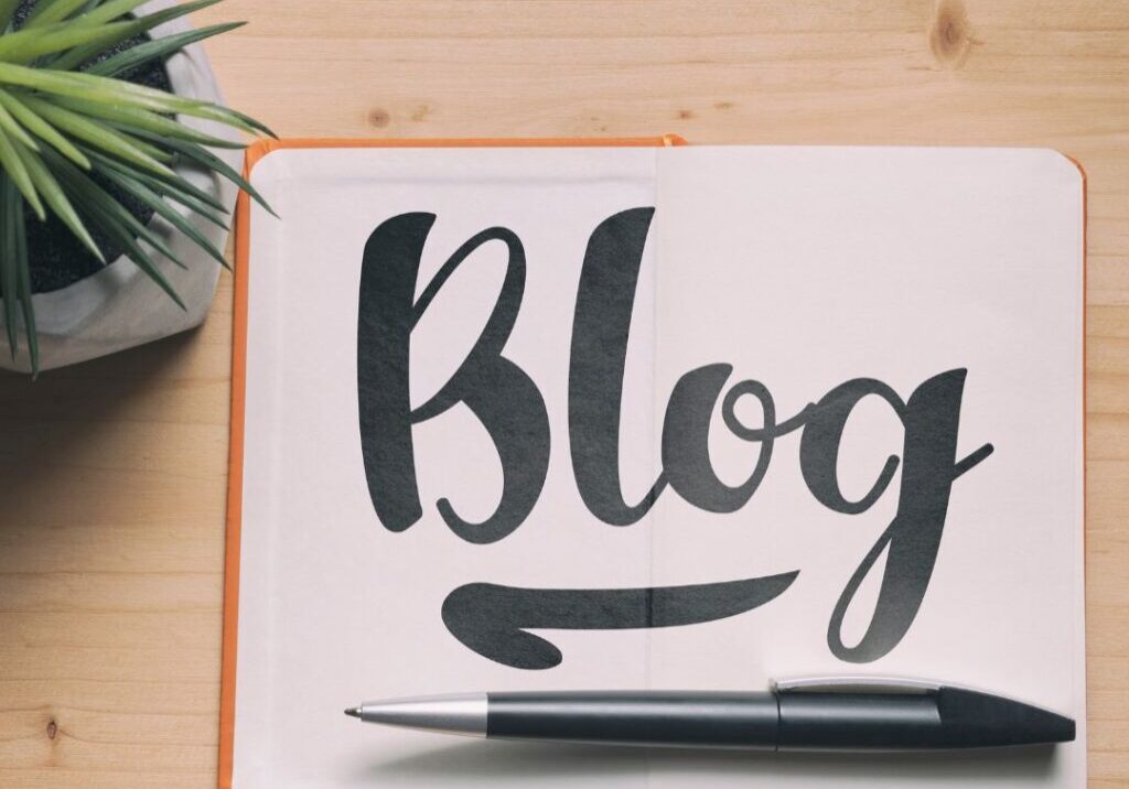 The word "Blog" is written in bold sharpie on a notebook next to a potted succulent plant